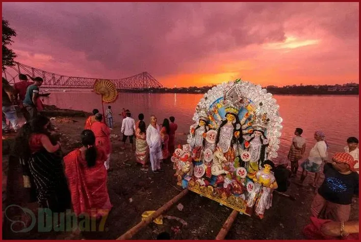 Durga idol being taken for immersion during Durga Puja visarjan by the riverside in Bengal, with devotees gathered at sunset.